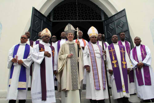La obispa primada Katharine Jefferts Schori, el obispo diocesano de Haití Jean Zaché Duracin, a la derecha, el obispo sufragáneo de Haití Ogé Beauvoir, a la izquierda, y algunos clérigos posan en las gradas de la parroquia del Espíritu Santo en Cabo Haitiano luego de la eucaristía del 14 de diciembre. Foto de Lynette Wilson/ENS.