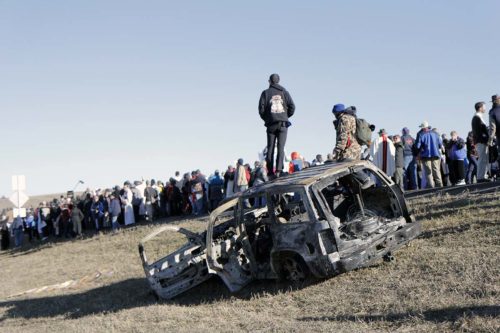 A man stands on a burnt-out SUV as interfaith witnesses share testimony and commit to carrying with them home the message from Standing Rock. Photo: Lynette Wilson/Episcopal News Service 